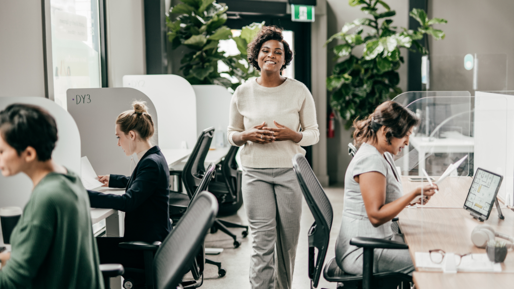 Partnering with professionals — modern workspace (1920×1080) Professional woman standing in a modern workspace; colleagues working at desks